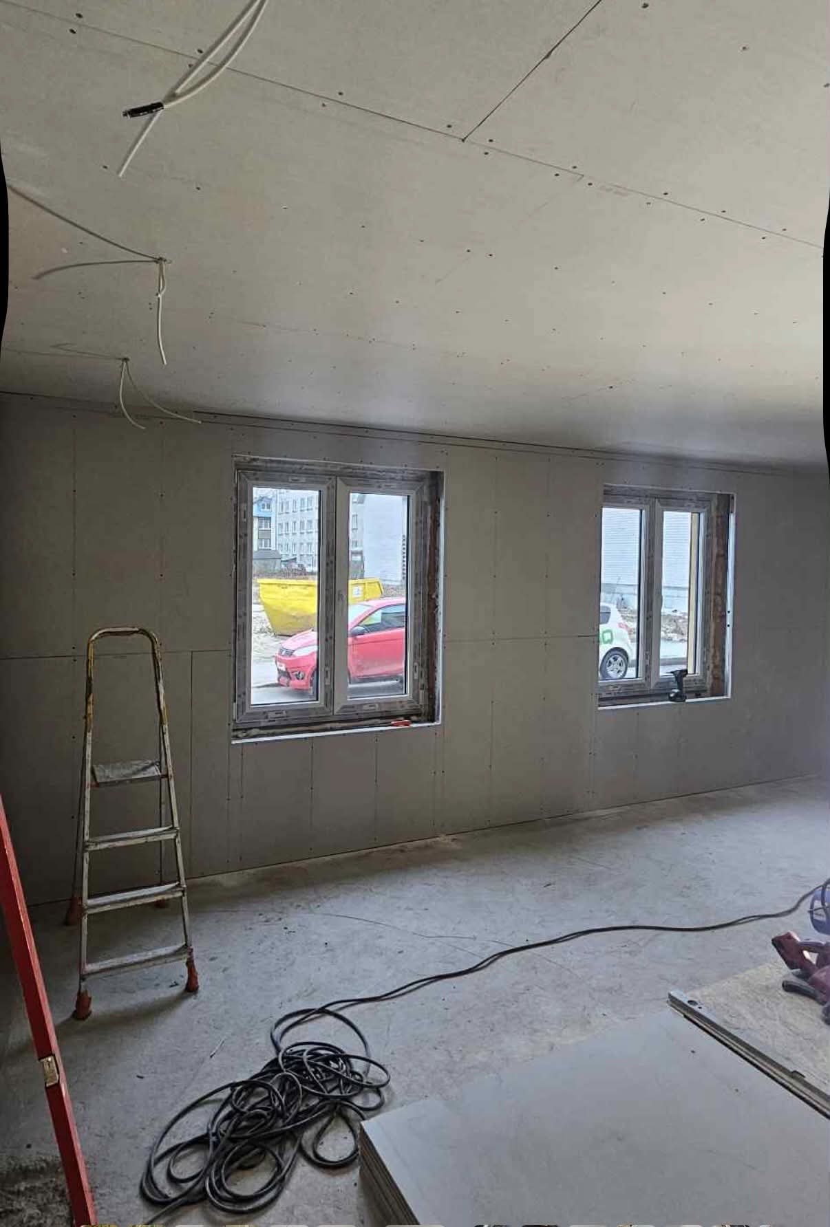 Room mid-renovation with new drywall walls and fresh windows